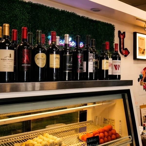 A display of red wine bottles above a refrigerated case with pastries and sweets.
