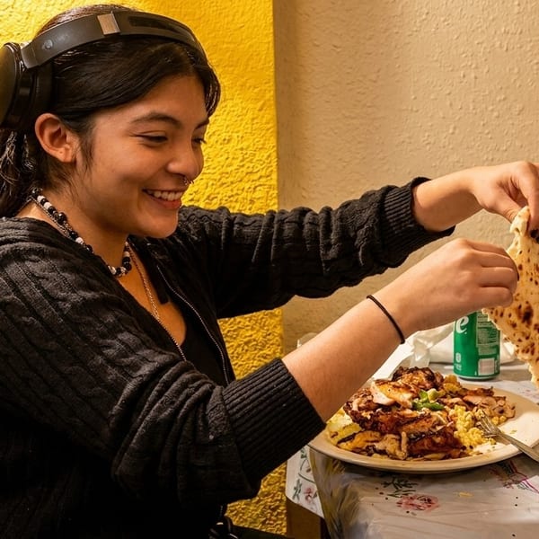 A smiling young woman with headphones eating chicken and rice with naan bread.