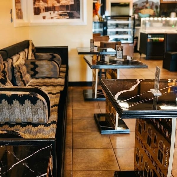 Restaurant interior with a long patterned sofa, black marble tables, and a counter in the background.