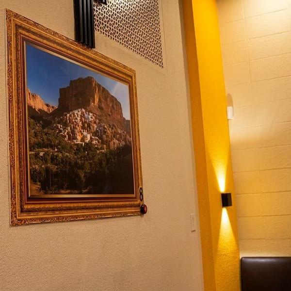 Two framed landscape paintings hang on textured walls, illuminated by modern wall sconces in a restaurant.