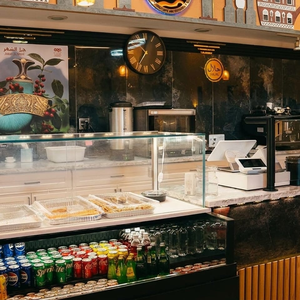 A cafe counter with a display case of pastries, a drink cooler, and a barista working behind the counter.