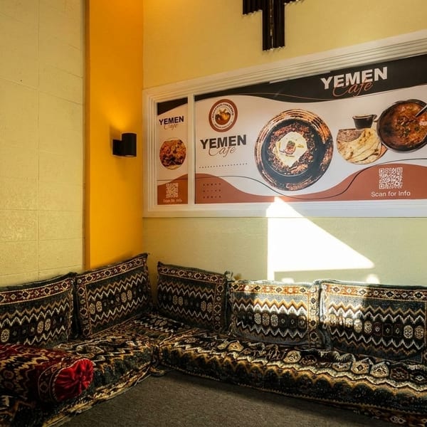 Cozy corner with patterned floor seating and cushions, a Yemen Cafe menu board on the wall.